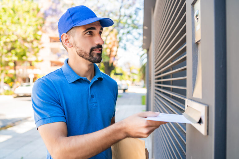 Close-up of a postman putting a letter in a house mailbox. Delivery postal service concept.